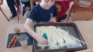 Chłopiec pędzelkiem wykopuje kości dinozaurów.