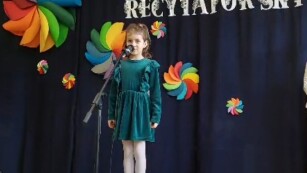 dziewczynka w zielonej sukience recytuje wiersz na scenie