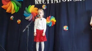 dziewczynka w czerwonej spodniczce i białej bluzce mówi wiersz na scenie